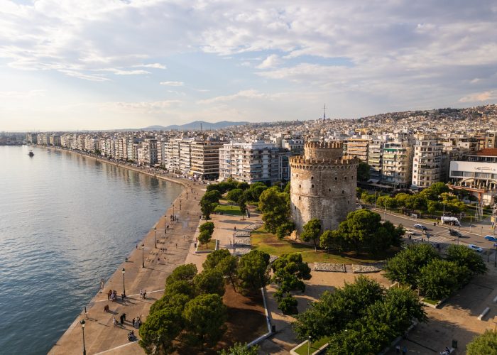 Aerial view of the White Tower in Thessaloniki, Greece, surrounded by lush greenery and the vibrant